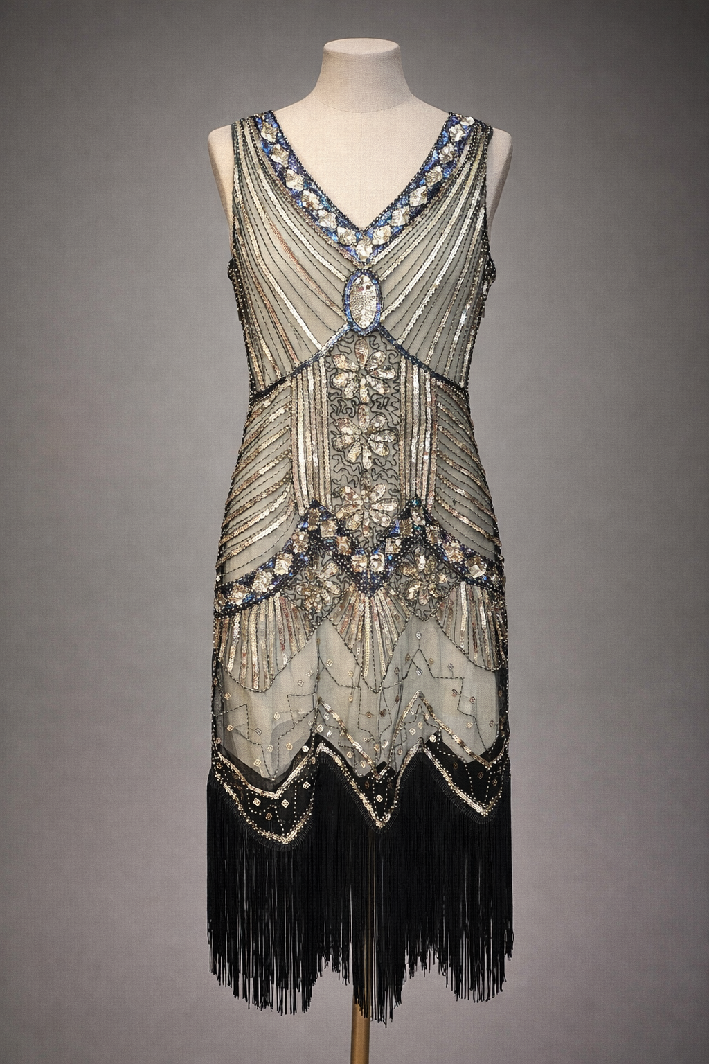 1920's Flapper dress with intricate beading and fringes on a mannequin against a gray background